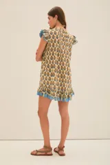 Vestido corto color crema con estampado floral en tonos azul y ocre. Tiene escote en V, mangas cortas con volados y falda con volados y terminación con guarda azul.