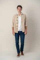 Sobre camisa color beige confeccionada en lino, de corte recto, con cuello clásico, manga larga con puños abotonados, cierre frontal con botones a tono, bolsillo de parche en el pecho y ruedo recto.