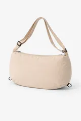 Bandolera color beige, con forma rectangular y extremos redondeados. Tiene una correa ajustable con hebilla negra y cierre de cremallera en la parte superior.