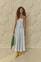 Vestido midi de jean celeste, con corte recto, sin mangas y escote recto. Presenta cierre frontal con botones y falda con ruedo desflecado.