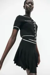 Saco corto negro en tejido de punto tupido con ribetes blancos en cuello, mangas y ruedo. Tiene cuello redondo, botones metálicos al frente y bolsillos superiores decorativos.