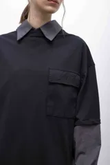 Remerón negro oversize con cuello camisero gris, mangas largas grises con puños elásticos, bolsillo con tapa en el pecho y logo bordado.