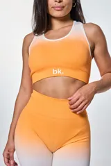 Conjunto deportivo de calza corta y top, color naranja con degradado a blanco. El top es de corte deportivo con logo "bk." en el frente.
