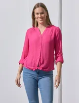 Blusa blanca de gasa marca Zac & Rachel, con cuello a la base, escote en V, abertura central con botones, bolsillo aplicado en el pecho y mangas largas regulables con presilla y botón. Tiene terminación opcional de nudo en el ruedo.