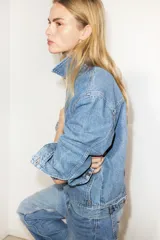 Campera de denim azul de algodón rígido con cuello, cierre delantero y canesú en la espalda. Modelo con puños abotonados, bolsillos delanteros con solapa y bolsillo interior de parche en el pecho. Trabillas ajustables con botones en la parte posterior del bajo.