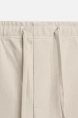 Pantalón de jogging color beige confeccionado en tejido de mezcla de algodón. Cuenta con cintura elástica ajustable con cordón, bolsillos frontales y traseros.