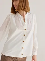 Camisa color crudo de corte recto y manga larga, con cuello mao y botones de madera. Presenta detalles de bordado calado en el frente.