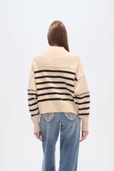 Sweater beige con rayas horizontales negras, cuello alto y corte holgado.