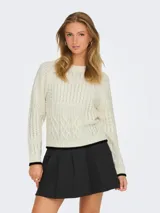 Sweater de punto color crema con diseño de trenzas y punto arroz. Tiene cuello redondo y mangas largas con puños y bajo acanalados con borde negro.