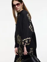 Vestido camisero negro con bordados dorados de motivos geométricos.