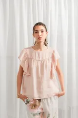 Blusa color rosa pálido de lino con volados en las mangas, corte ancho, cuello redondo y detalle de calado en el canesú.