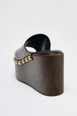 Mules de cuero marrón con plataforma de madera y detalle de tachas doradas.