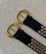 Cinturón negro de cuero ecológico con hebilla dorada y múltiples ojales dorados.