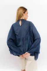 Camisa azul de algodón con cuello alto y mangas largas acampanadas con detalles de puntilla.