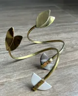 Brazalete rígido abierto, hecho a mano en bronce o alpaca, con terminaciones en forma de media luna y hojas.