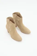 Bota corta de cuero gamuzado color beige, estilo texana, con taco medio de 6 cm y diseño de mariposa en los laterales.