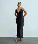 Vestido largo negro de satén con escote pronunciado en V y detalle de recorte central en el busto. Posee breteles finos ajustables y silueta alargada con leve cola en el ruedo.