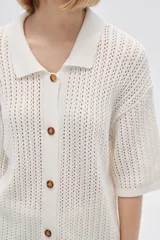 Remera de punto calado color beige, con cuello polo, mangas cortas y cierre frontal con botones.