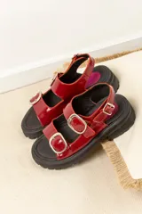 Sandalias rojas charoladas con hebillas plateadas, plataforma track negra y plantilla fucsia.