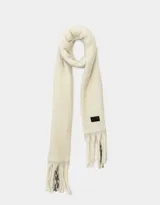 Bufanda tejida color crema con flecos en los extremos y etiqueta de cuero sintético negra.
