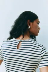 Remera de punto acanalado a rayas horizontales blancas y azul marino, con cuello redondo adornado con strass brillante. Presenta abertura de cerradura con botón en la nuca y bajo recto. Corte ajustado.