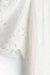 Vestido corto blanco de crepé con secciones de broderie, cuello camisero, botones ocultos, mangas cortas abullonadas, cinturón extraíble y ribete festoneado.