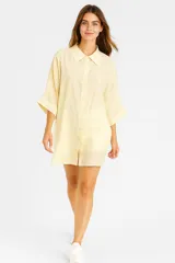 Túnica amarilla con rayas verticales, cuello camisero, cierre frontal con botones y mangas cortas.