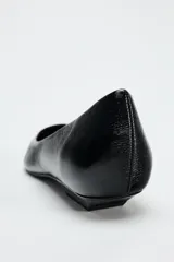 Zapato plano de charol negro con punta fina y suela baja.