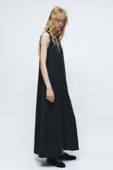 Vestido midi negro de cuello redondo y sin mangas. Corte amplio y fluido, con bolsillos laterales ocultos y cierre trasero con cremallera invisible.