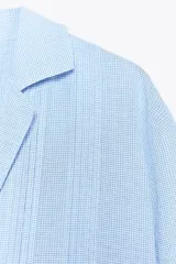 Camisa oversize celeste con textura de algodón, cuello solapa y manga larga. Presenta pliegues delanteros y bajo asimétrico.