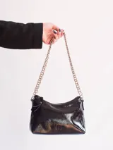 Cartera negra de cuero charol con forma de media luna y correa de cadena dorada.