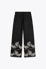 Pantalón culotte negro de lino y viscosa con bordados florales en el ruedo. Tiene tiro medio, cintura con trabillas, bolsillos laterales y cierre frontal con cremallera y botón.