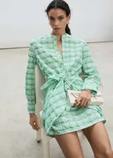 Vestido corto camisero con estampado de cuadros verdes y celestes, cuello mao, mangas largas abotonadas y lazo en la cintura.