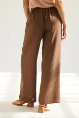 Pantalón de lino azul de corte palazzo con botón decorativo en la cintura.