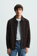 Sobrecamisa marrón de cuero gamuzado, corte recto, con cuello clásico, cierre frontal con botones, mangas largas con puños abotonados y bolsillos de parche en el pecho.