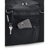 Bolso tote deportivo Under Armour color negro, con asas de hombro y logo de la marca en el frente. Presenta un bolsillo exterior con cierre y malla, y detalles de herrajes en forma de 'D' en los laterales.