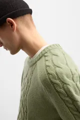 Sweater verde claro de punto con cuello redondo y mangas largas. Presenta diseño de trenzas en el centro y en las mangas.