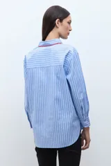 Camisa de manga larga, corte oversize, color celeste con rayas verticales blancas. Presenta un detalle de bordado en color rojo/fucsia a lo largo del cuello y la abertura frontal.