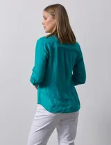 Blusa blanca de gasa marca Zac & Rachel, con cuello a la base, escote en V, abertura central con botones, bolsillo aplicado en el pecho y mangas largas regulables con presilla y botón. Tiene terminación opcional de nudo en el ruedo.