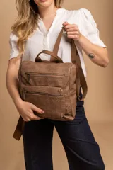 Mochila mediana color marrón de símil cuero con asa superior y correas ajustables. Tiene dos compartimentos principales con cierre y dos bolsillos frontales con cierre.