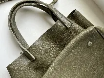 Cartera tipo tote bag color bordó, confeccionada en cuero con textura granulada. Tiene doble asa corta de mano y asa larga extraíble con diseño de tachas para usar como bandolera.