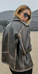 Chaqueta de cuero ovino color marrón, con cuello clásico, cierre asimétrico con cremallera, solapas con botones a presión, múltiples bolsillos con cremallera y cinturón ajustable en la cintura.