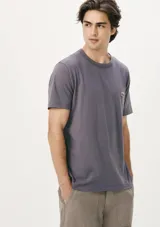 Remera gris con cuello redondo y manga corta. Presenta un pequeño parche con logo en el pecho.