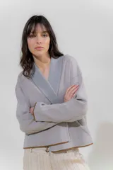 Chaqueta de punto color crudo con solapa ancha acanalada terminada con cadenetas en contraste negro. Tiene calce relajado, hombros caídos, largo a la cadera y manga larga.