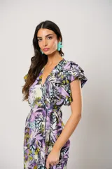Vestido largo con estampado floral en tonos lila, verde y negro. Tiene escote en V, mangas cortas con volados y corte cruzado con lazo en la cintura.