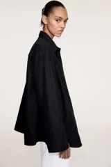 Camisa negra oversized de algodón con cuello clásico, abotonadura frontal, mangas largas con hombros caídos, puños con abertura y bajo recto.