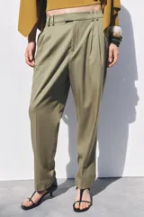 Pantalón color verde oliva de tiro medio con cintura con trabillas, bolsillos laterales, pinzas delanteras y raya planchada. Cierre frontal con cremallera, botón y ganchos metálicos.