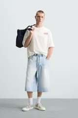 Camiseta blanca de corte holgado, cuello redondo y manga corta. Estampado frontal con la frase "Gourmet Groove LLC" en color fucsia.