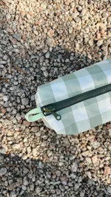 Necessaire rectangular de tela estampada a cuadros verdes y blancos, con cierre superior y etiqueta verde con logo.