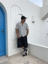 Camisa tejida a rayas verticales blancas y negras, de manga corta y cuello solapa.